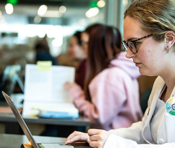 Saint Joseph's University PCP student wearing PharmD white coat working on laptop