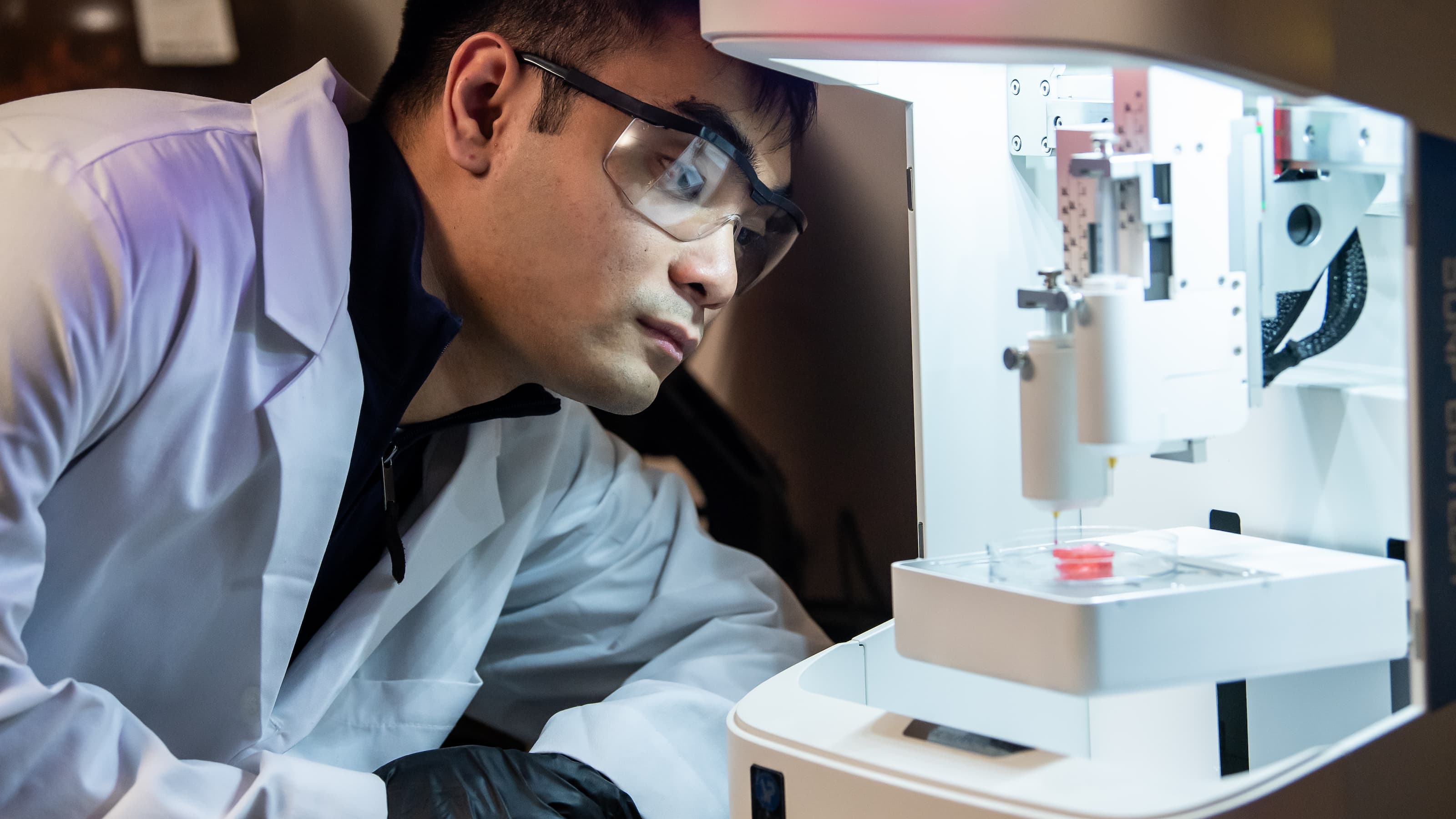 A student in a lab coat closely inspects a medical device.