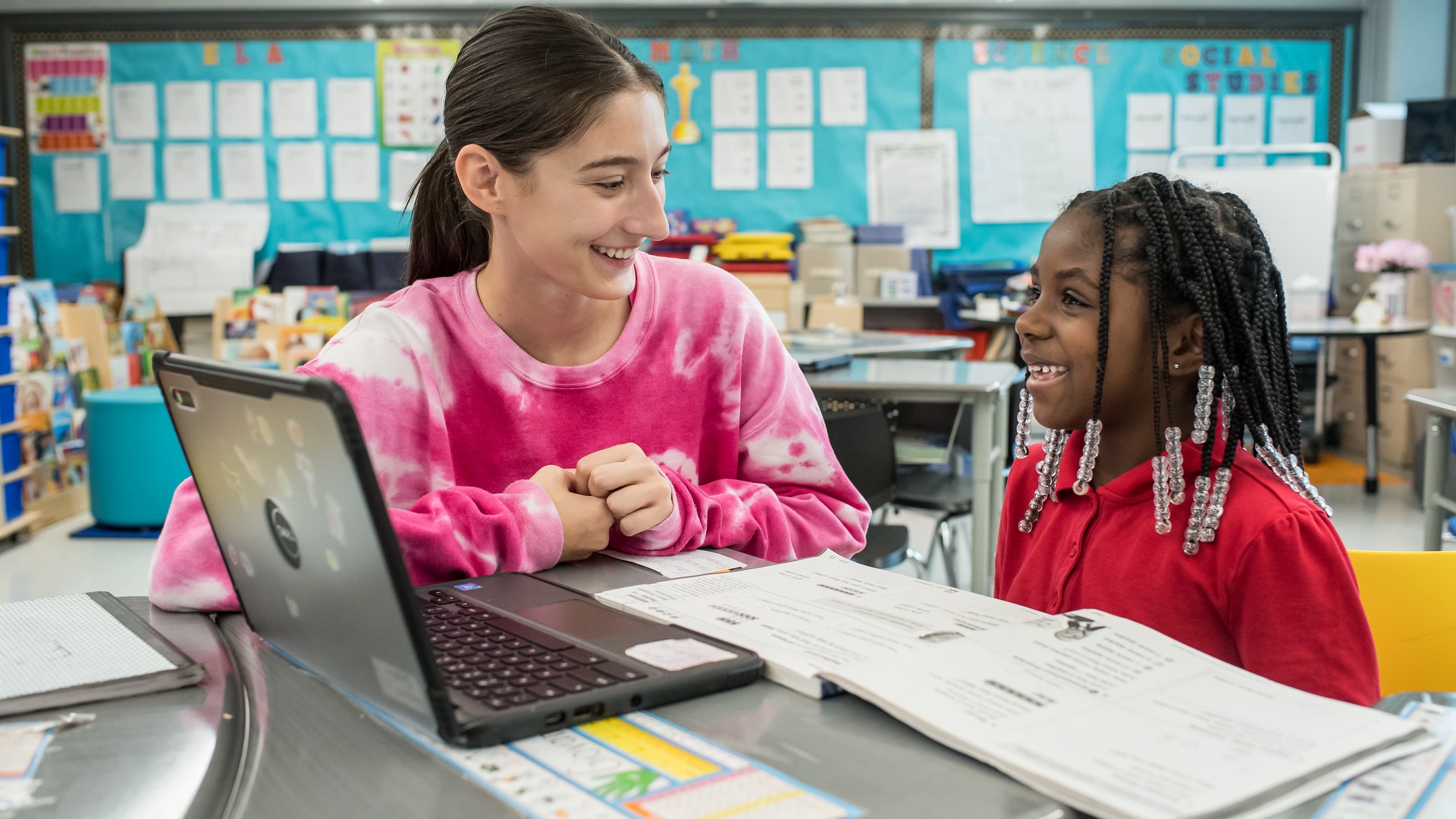 A college student sits with an elementary student in a classroom. 