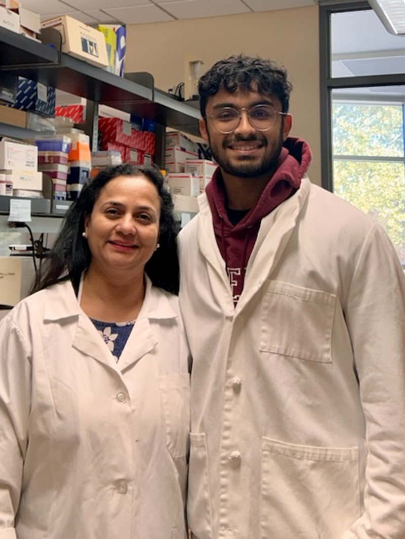 Eric Lalu (right) with Professor Bela Peethambaran in lab wearing white lab coats 