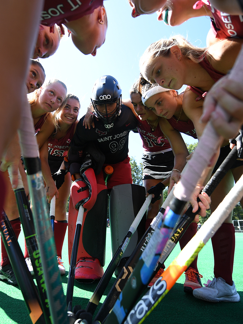 Saint Joseph's field hockey team in huddle with sticks coming together