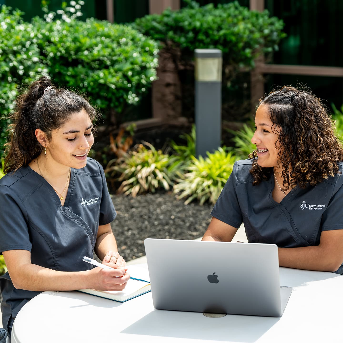 Two female Saint Joseph's nursing students sitting at table outside working on laptop