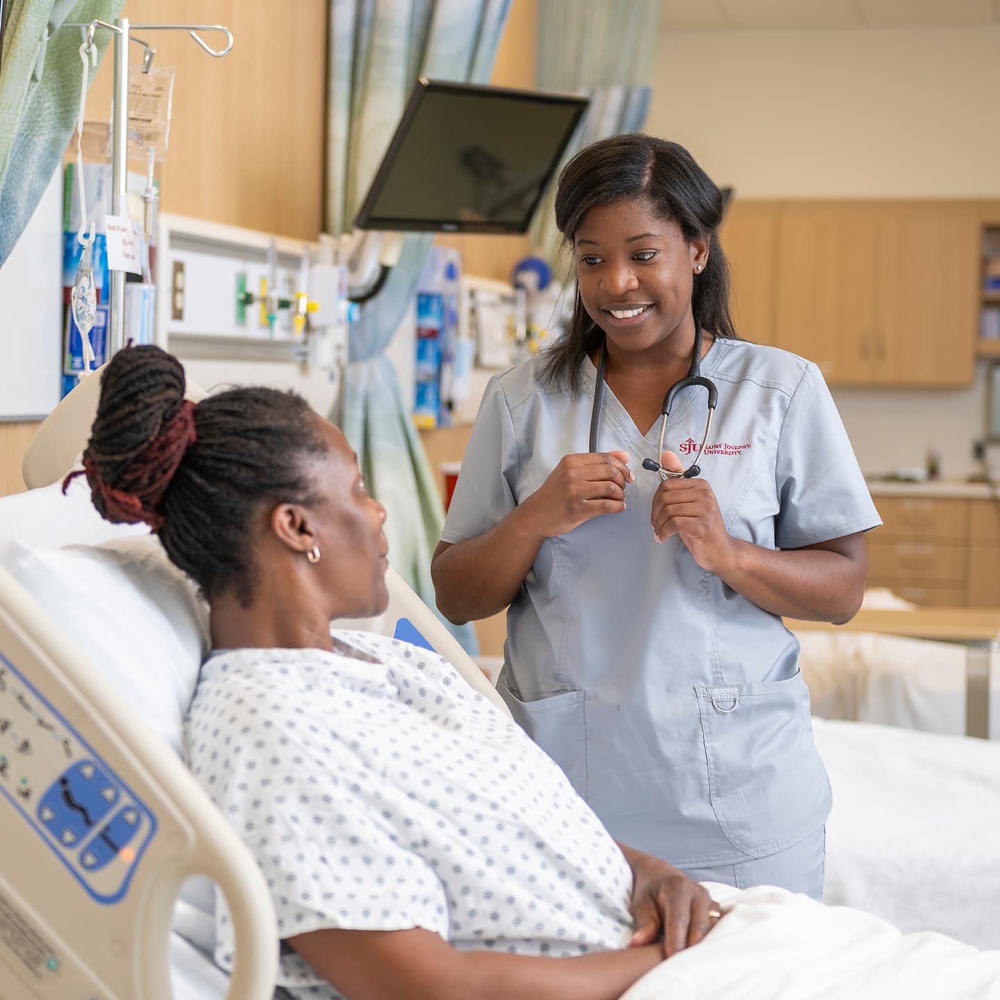 Female nurse standing next to female patient in hospital bed 