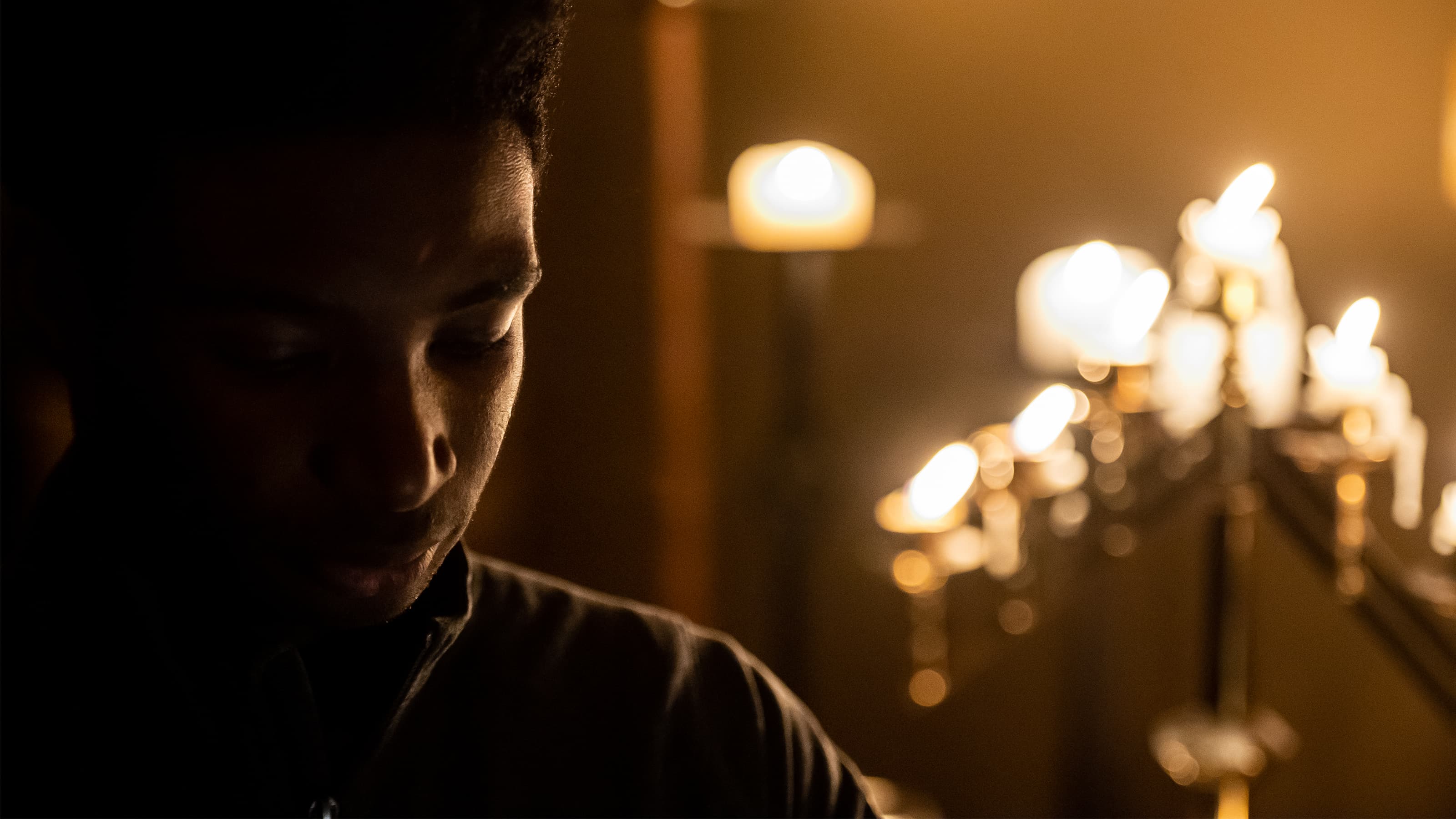 Close up of a male in a church in front of candles