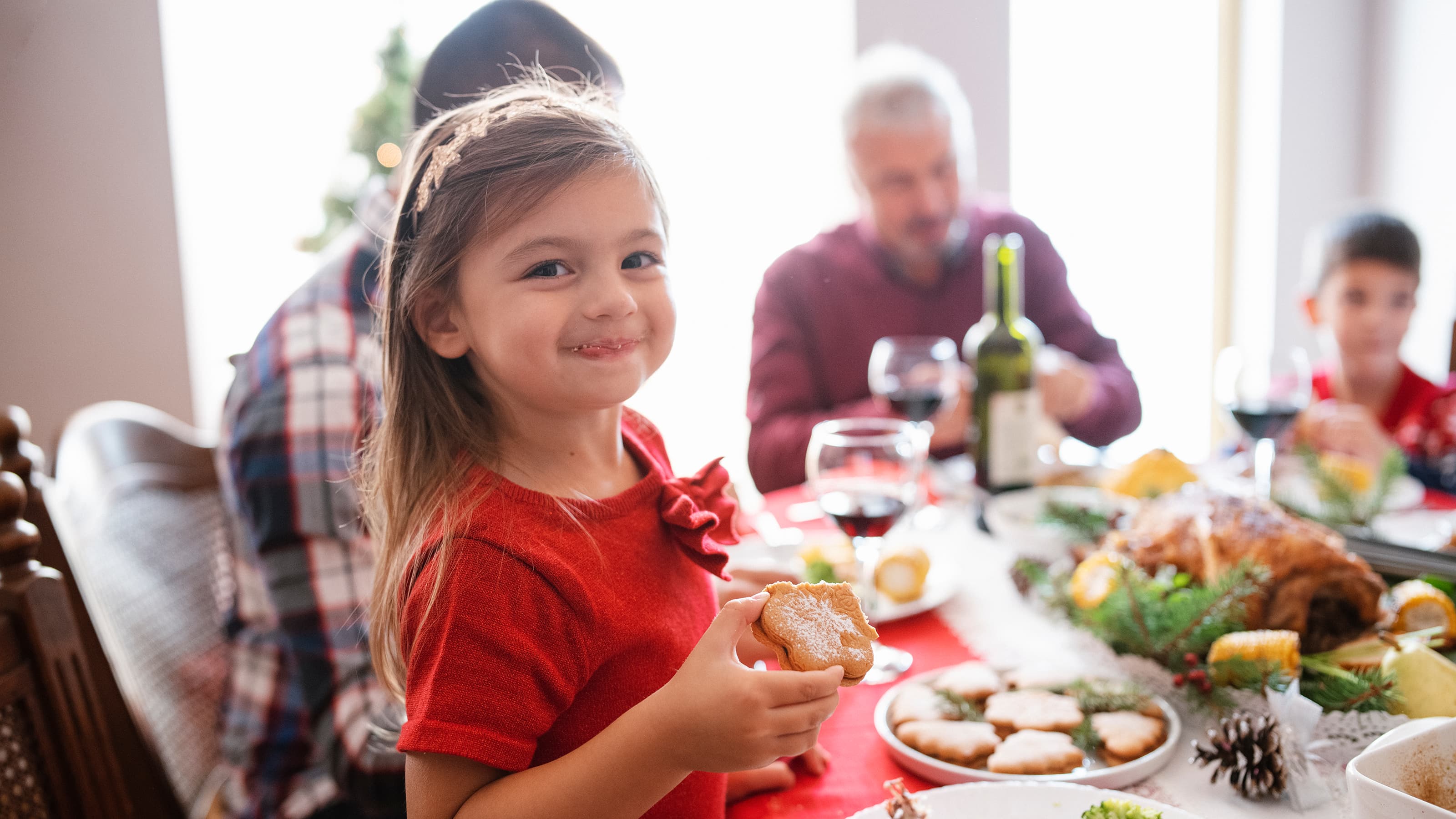 Happy girl eating a cookie at a holiday dinner with family