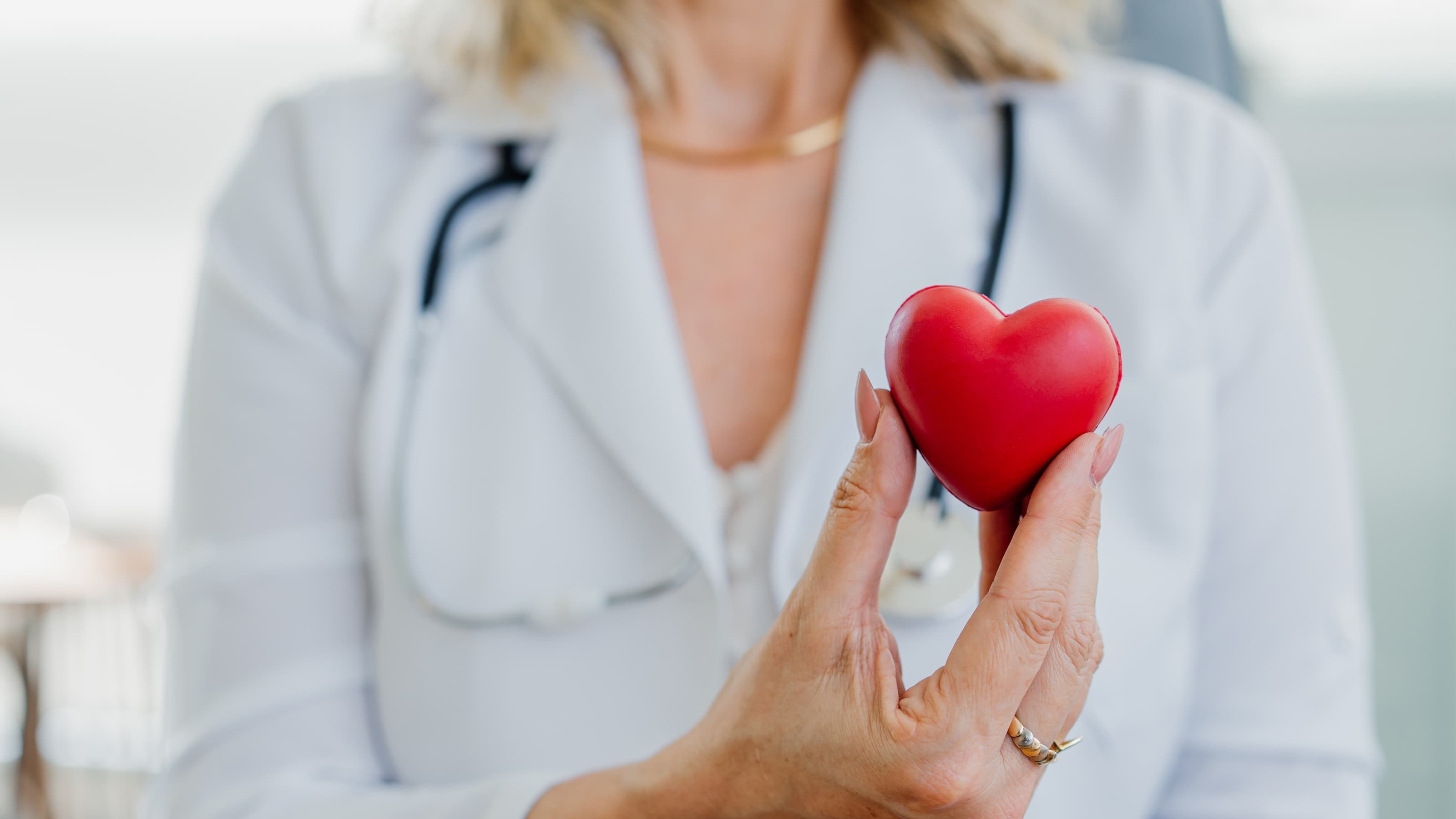 A doctor with a stethoscope holds a small red heart