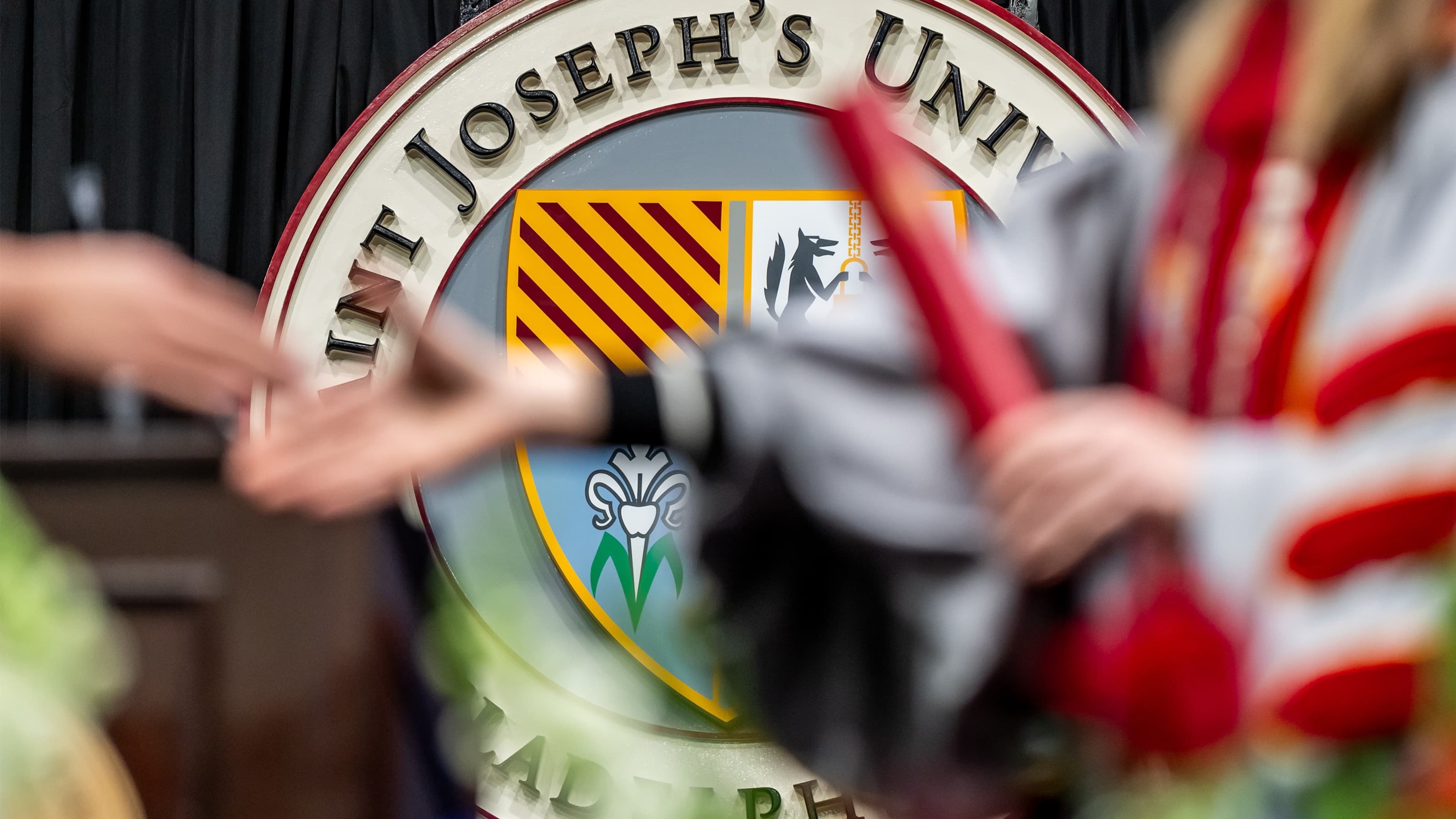 A student receives a diploma in front of the Saint Joseph's University crest.