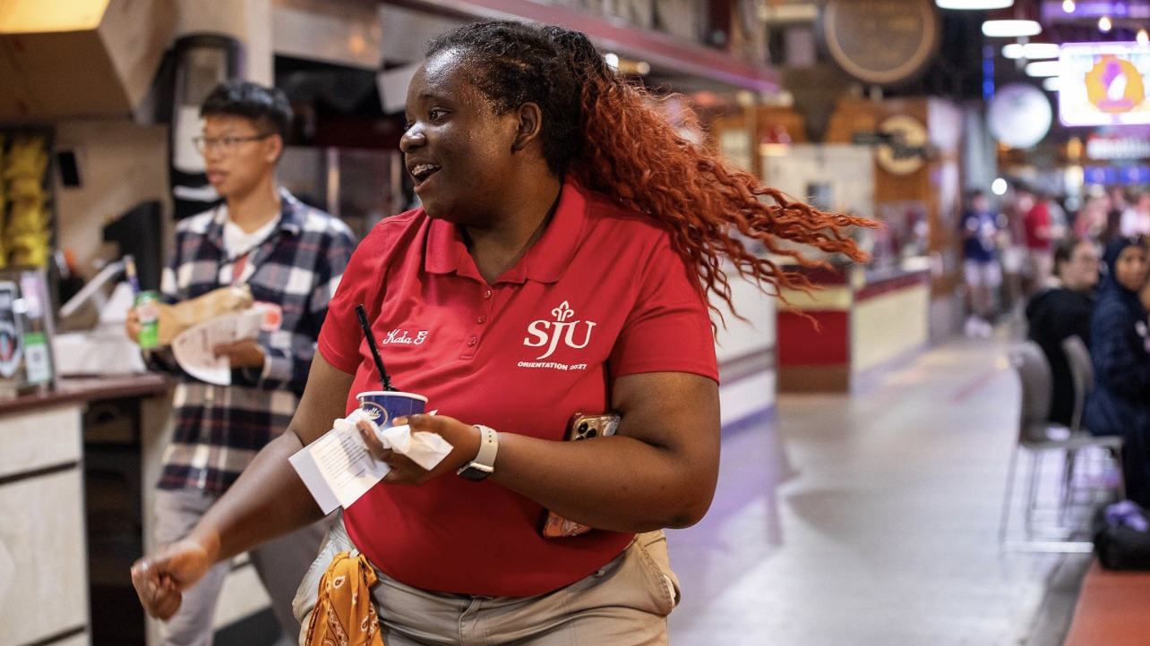 Kaia Grant wearing red orientation shirt dancing in Philadelphia Reading Terminal Market