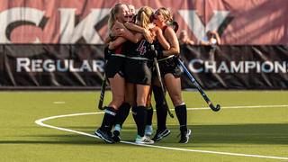 Saint Joseph's field hockey players group hugging and cheering in the middle of the field