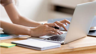female student's hands typing on laptop