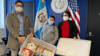 Two members of the Guatemalan Consulate present a pregnant woman with a baby box full of supplies.