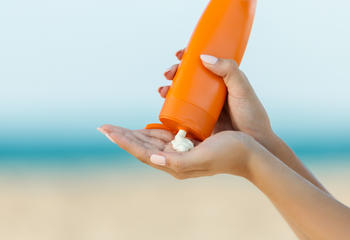 A woman pouring sunscreen into her hand on the beach. 