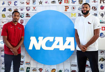 Saint Joseph's Xzayvier Brown and Phillip Lawrence-Ricks in front of blue NCAA sign and wall of basketball team logos