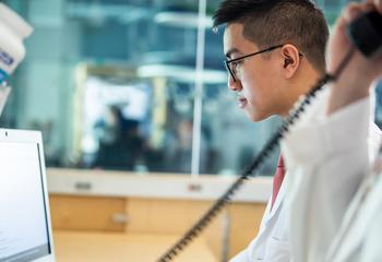 Male student in white coat typing at a computer in a pharmacy