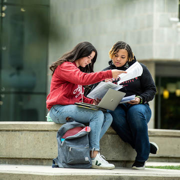 Female students working on laptop together outside Saint Joseph's library