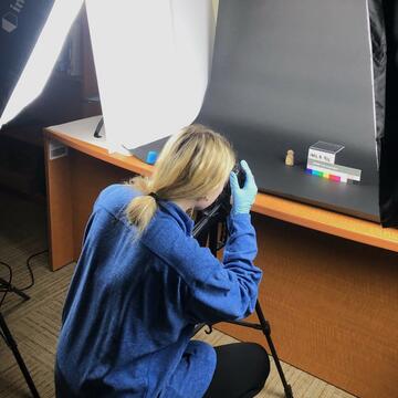 Student photographing a museum artifact against a dark backdrop