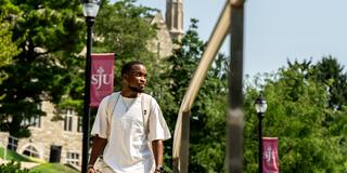 Male student walking on campus with barbelin building in the background
