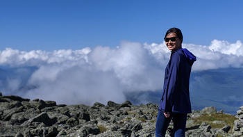 Dawn Cai standing on a mountain looking back at the camera